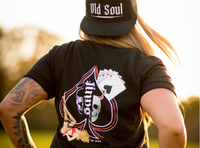 Person wearing a black t-shirt with a logo and 'Old Soul' cap outdoors.