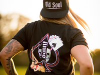 Person wearing a black t-shirt with a logo and 'Old Soul' cap outdoors.